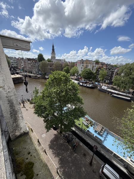 This photo captures a beautiful, sunny afternoon view over the Oudeschans canal in Uilenburg, Amsterdam, showcasing historic canal houses and houseboats
